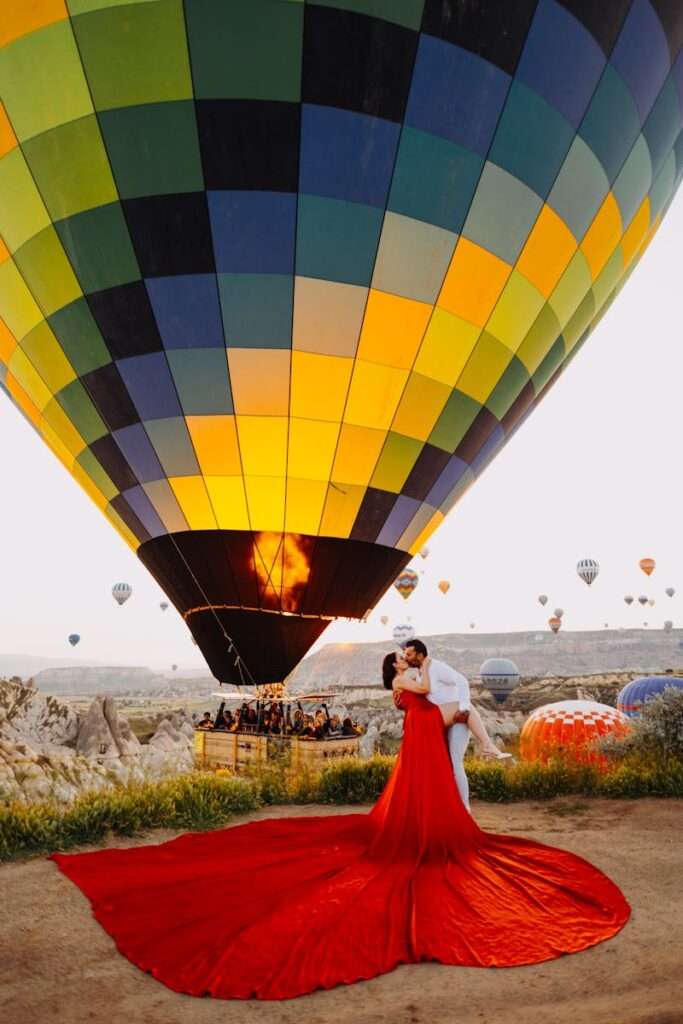 Couple shares a romantic kiss under a vibrant hot air balloon in Cappadocia, Turkey.