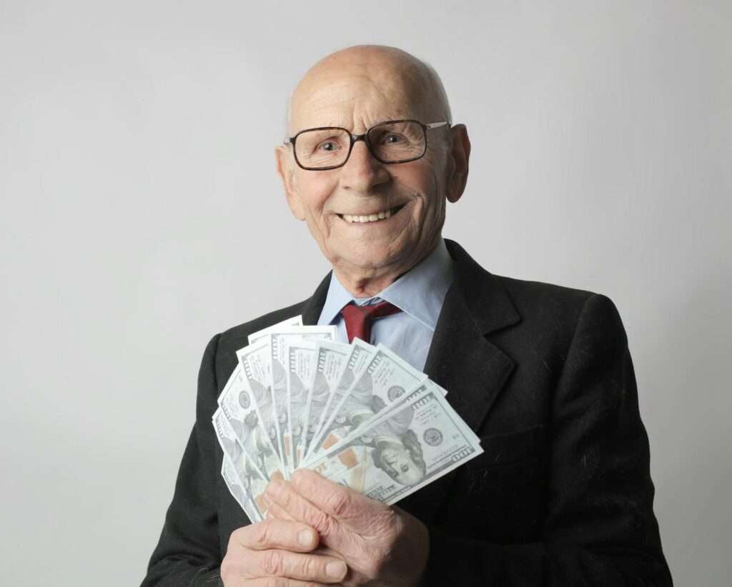 Senior man in a suit with glasses holding US dollars, symbolizing wealth and savings.