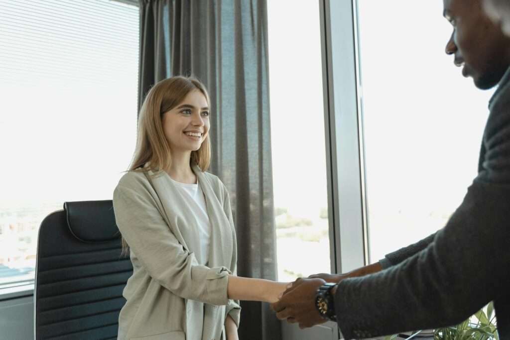 Woman smiling and shaking hands at a business office, signaling a successful job interview.