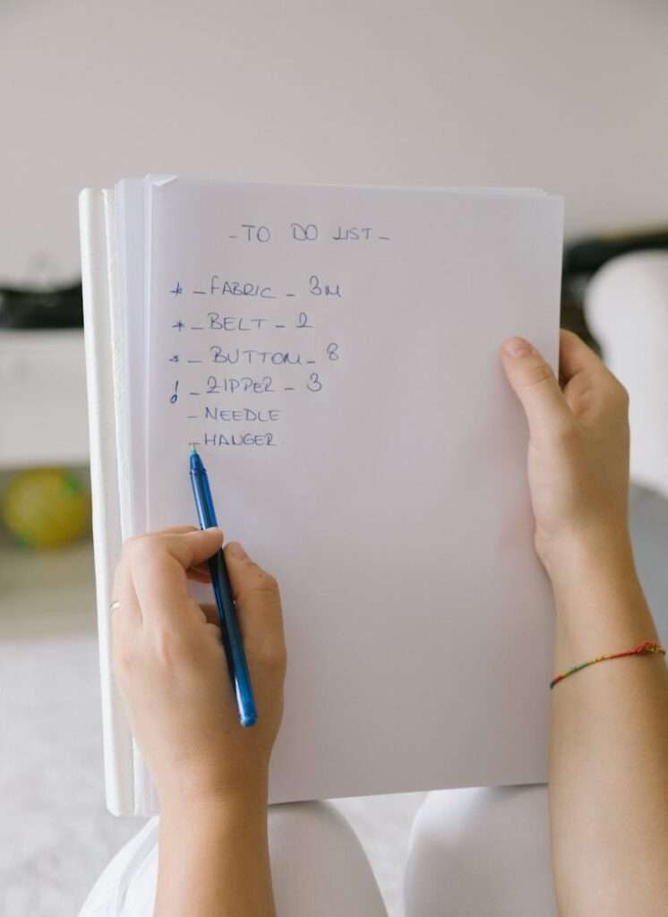 A person writing a to-do list on paper with a pen indoors.