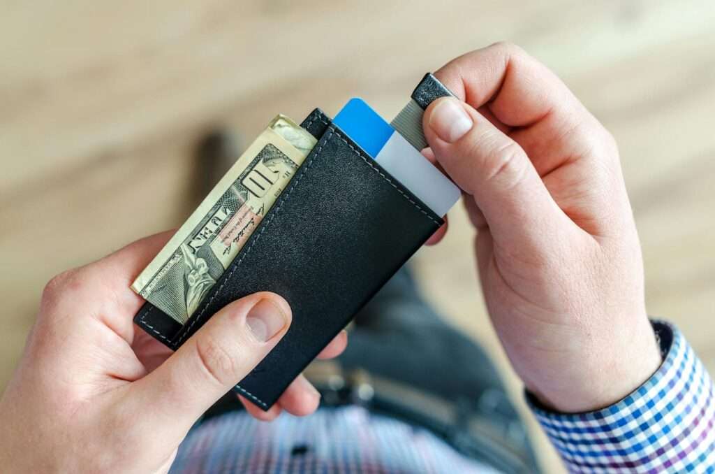 Close-up of a man's hands holding a wallet with cash and credit cards, indicating financial management.