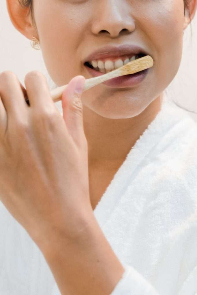 A person brushing their teeth with an eco-friendly bamboo toothbrush, promoting oral hygiene.