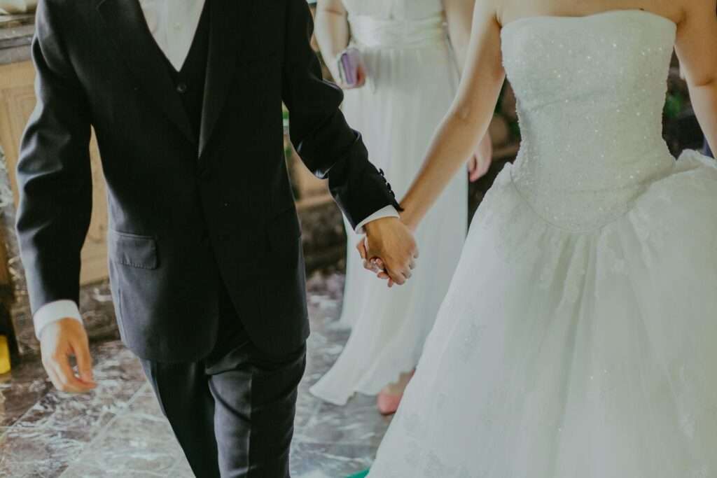 A romantic moment capturing a bride and groom holding hands in elegant wedding attire indoors.