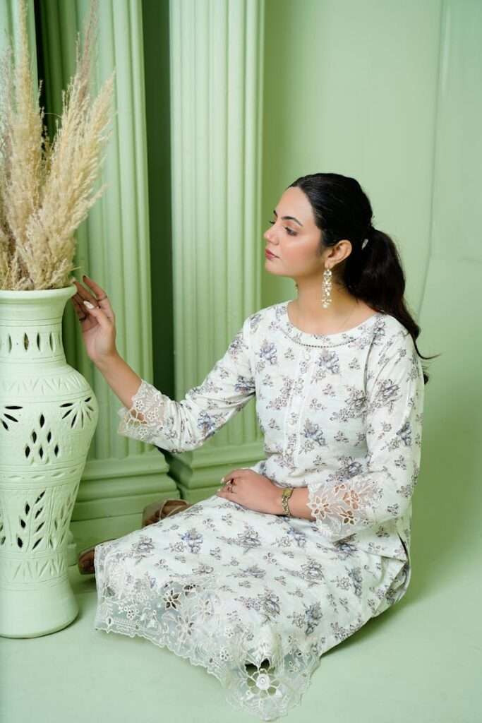 Stylish woman in an embroidered dress interacts with a decorative vase in a serene setting.