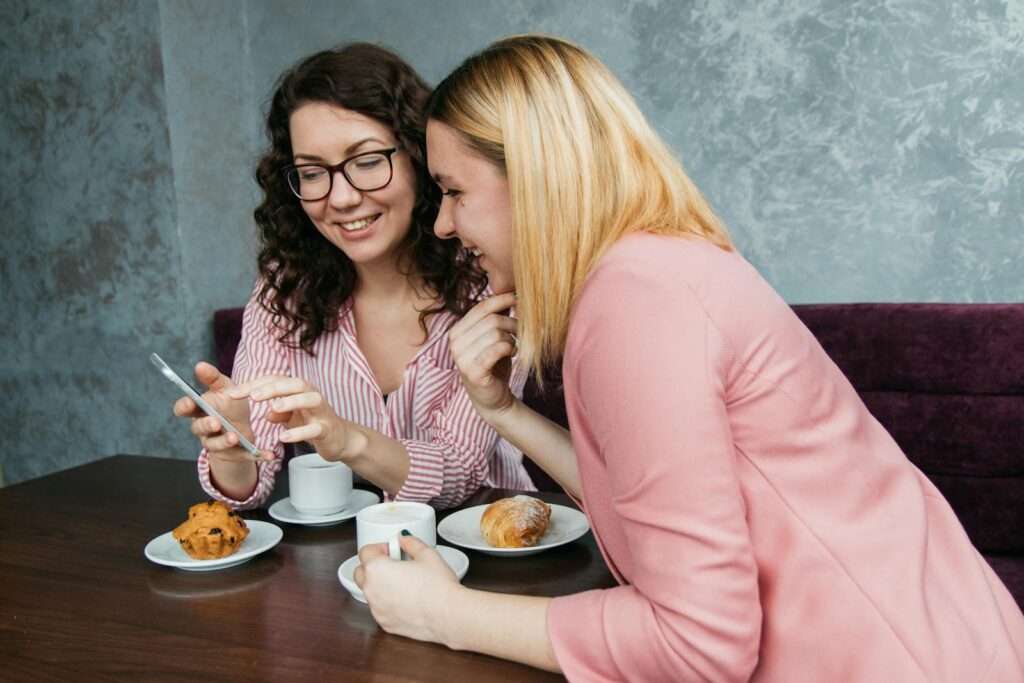 Two women sharing a fun coffee break, enjoying pastries and laughter in a cozy setting.