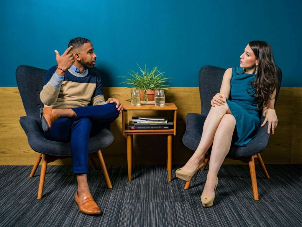 Two professionals in business attire engage in a thoughtful discussion sitting in a stylish, modern room.