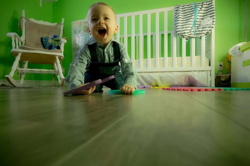 Delightful baby boy crawling on a wooden floor, playing happily in a vibrant green nursery.