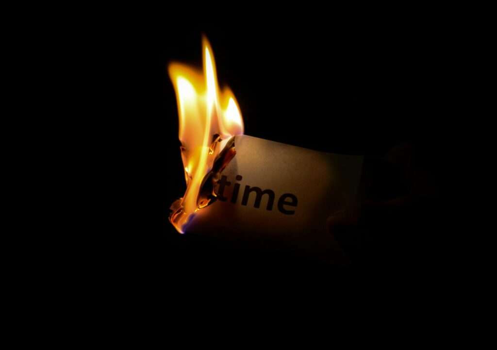 A close-up of a paper with the word 'time' burning against a dark background.