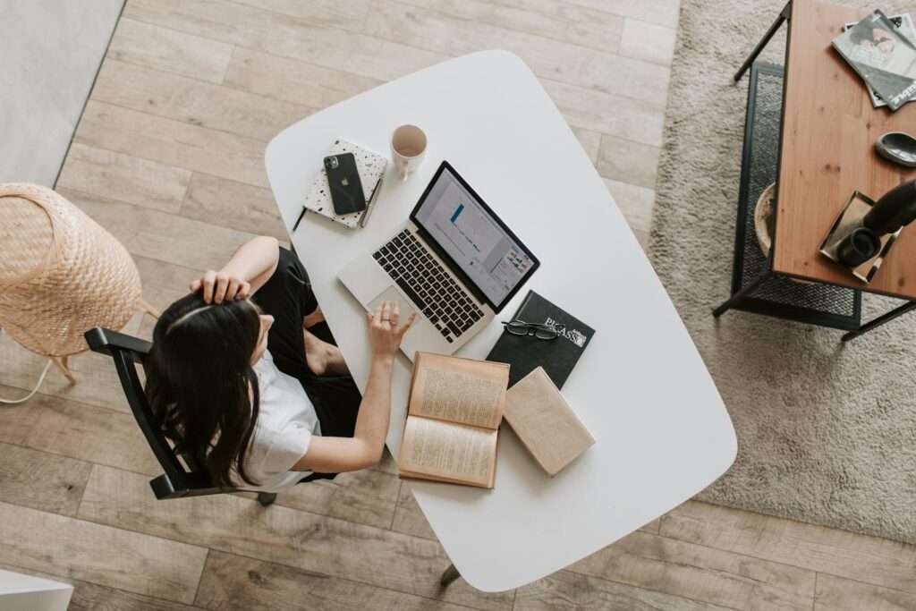 From above of young woman with long dark hair in casual clothes working at table and browsing netbook while sitting in modern workplace and touching hair