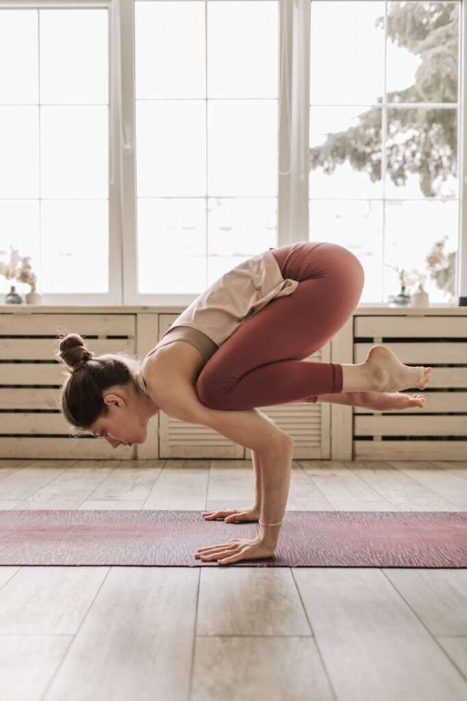 Woman performing advanced yoga pose indoors, emphasizing balance and strength.