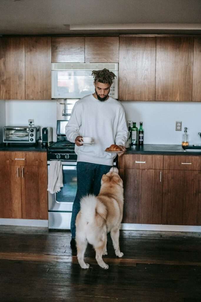 A man enjoys a quiet morning with coffee and a dog in his kitchen.