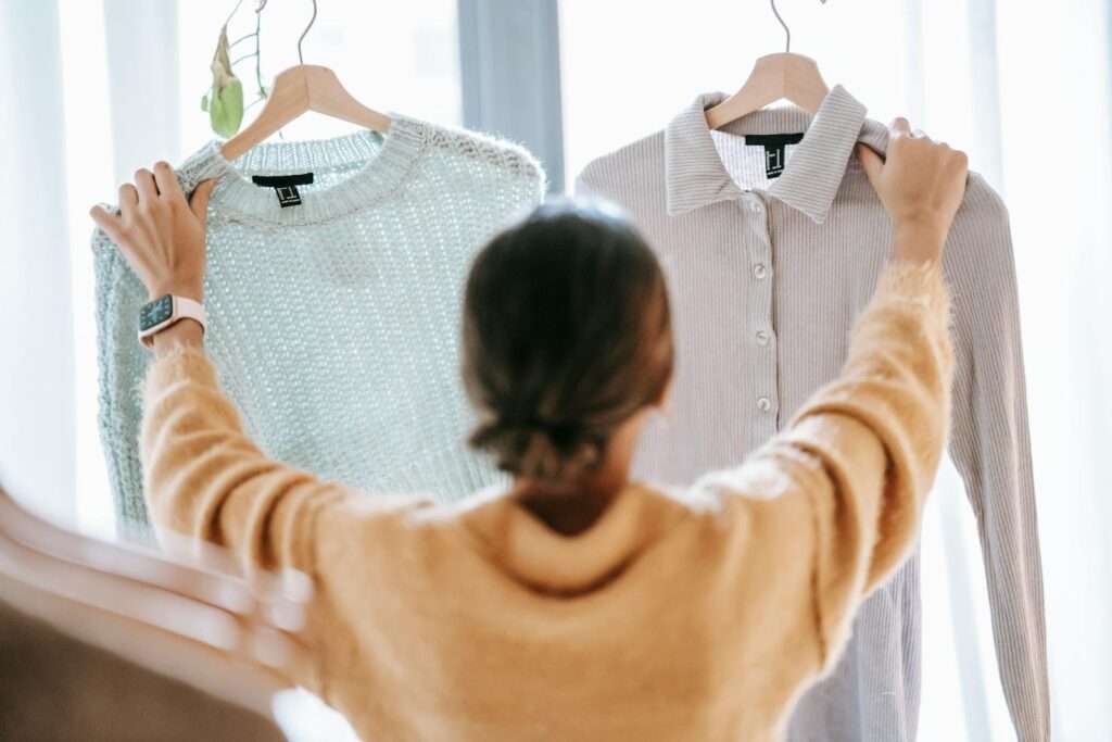 Woman deciding between two trendy sweaters in a modern boutique setting.