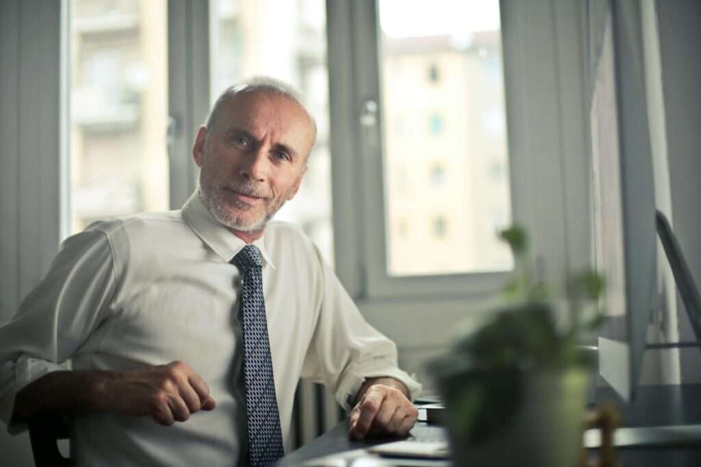 A mature man in professional attire smiling in an office setting.